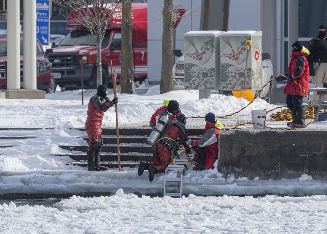 A diver from the TPS Marine Unit is helped ashore after attaching tethers to a car to remove it from the water. The car is pulled from the western channel metres away from the ferry to Billy Bishop Airport. One body was pulled earlier from the wreckage before the car was lifted out.